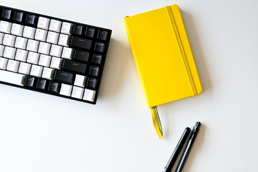 Yellow notebook and pens beside a keyboard on a white desk