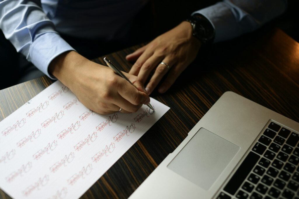 Person writing on a sheet of paper beside a laptop