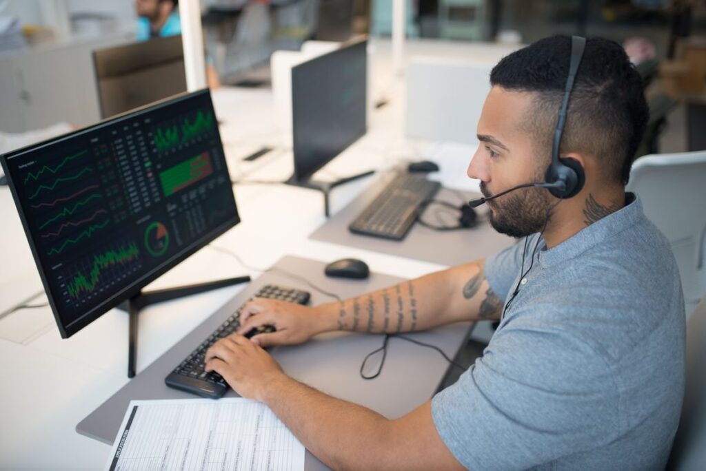 Man with a headset typing at a desk with chart screens