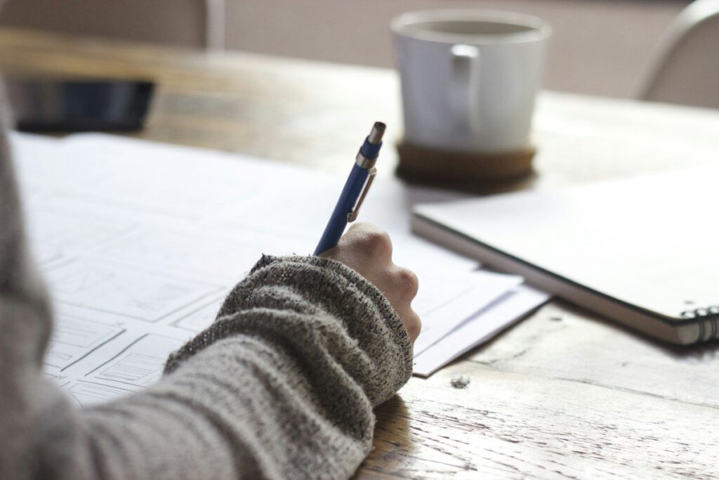Hand writing in a paper diary beside a coffee mug, keeping a trading journal after a session