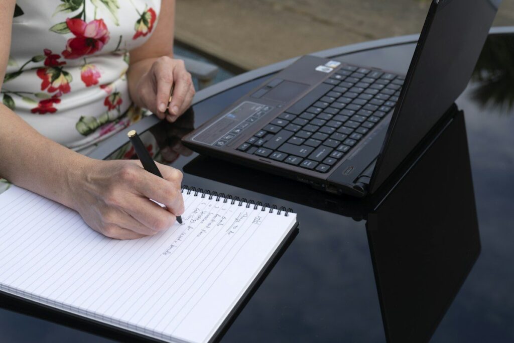 Person writing trading rules in a notebook beside a laptop, fixing which timeframes to check and in what order