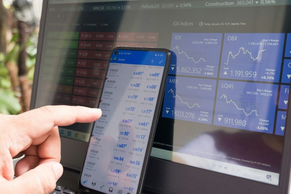 Finger pointing at a phone trading app in front of a screen of price charts