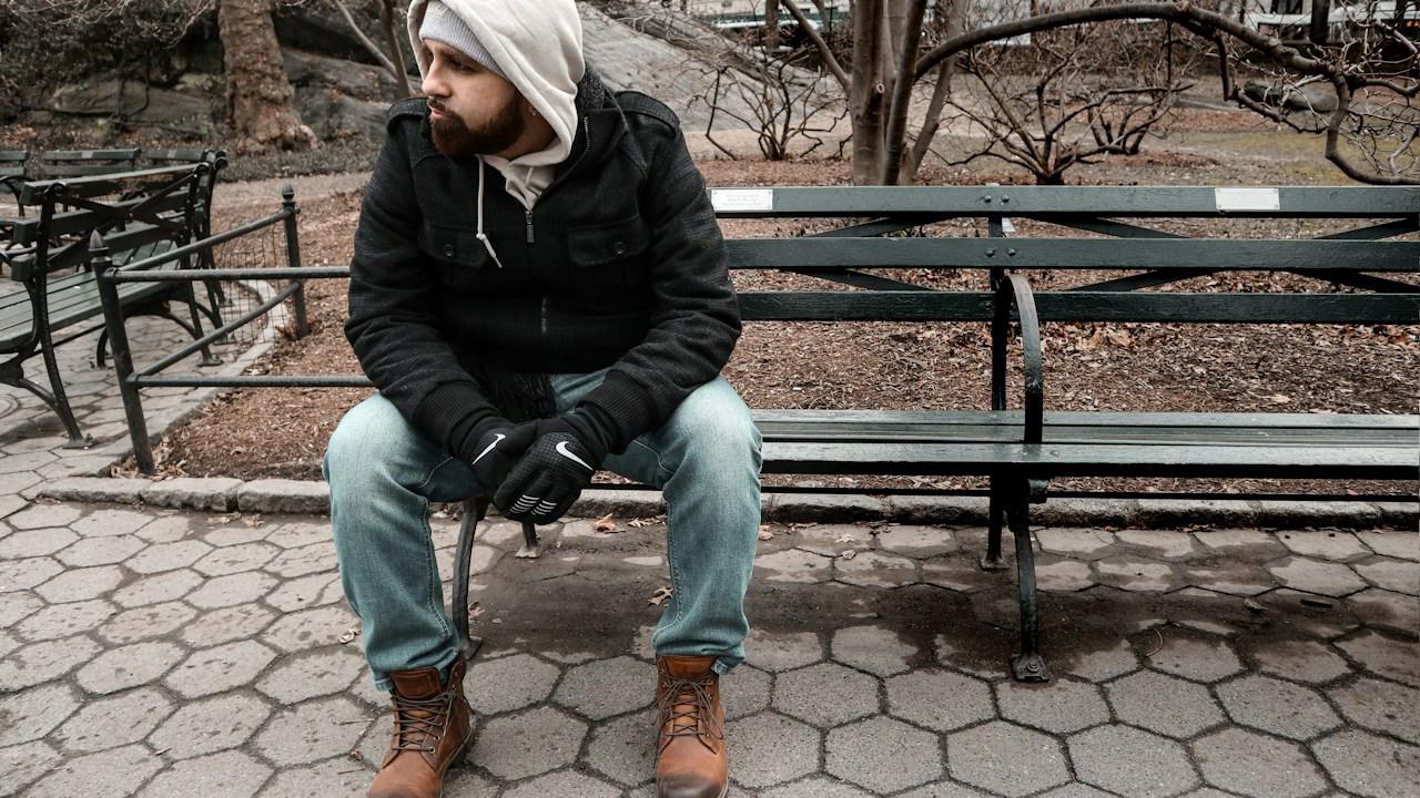 Man sitting alone on a park bench looking down, the low mood a trading drawdown and losing streak can bring