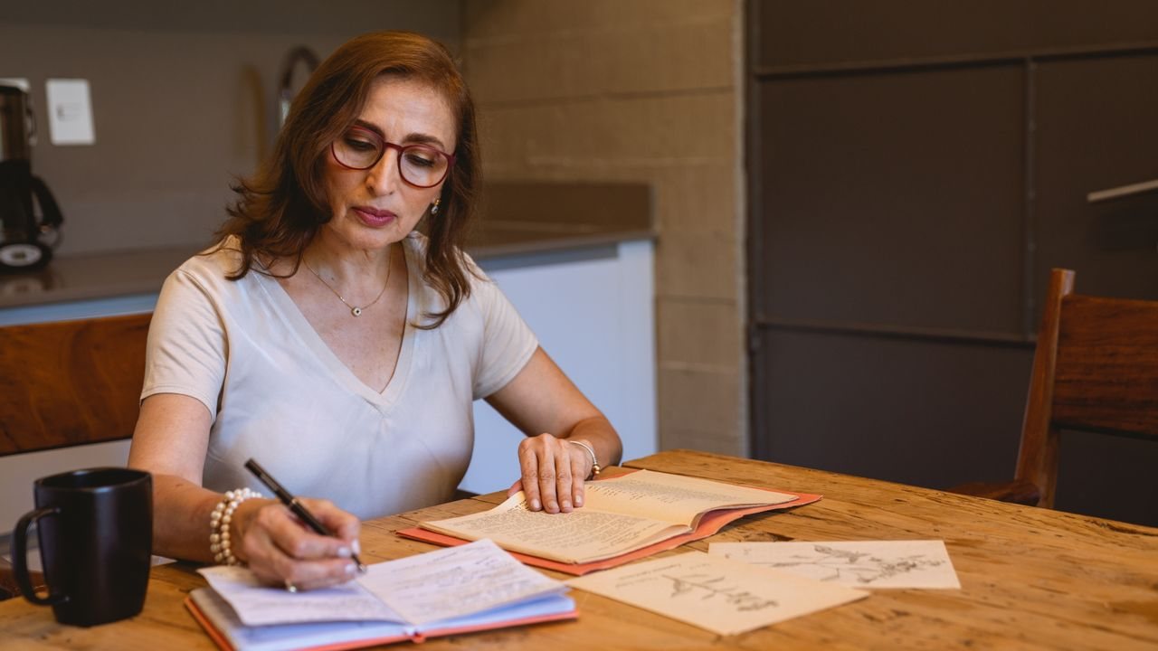 Person writing trade notes in a hardback notebook, keeping a trading journal for beginners