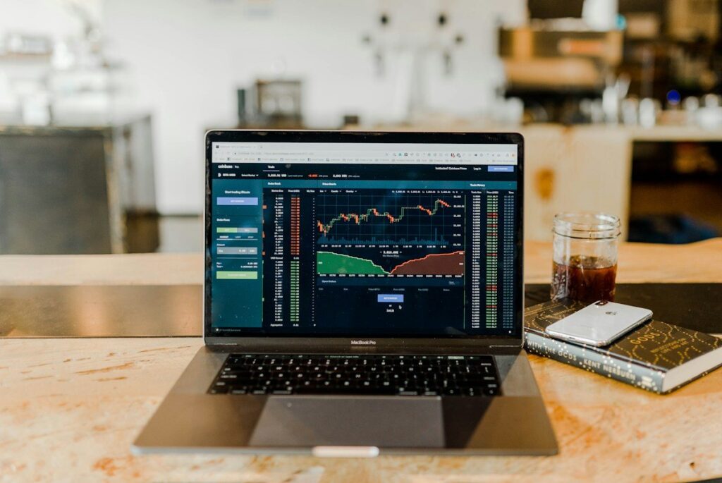 Laptop with a trading chart on a cafe counter beside a notebook