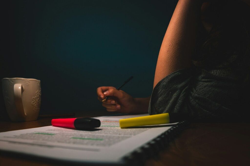 Hand writing on printed sheets beside highlighters at night