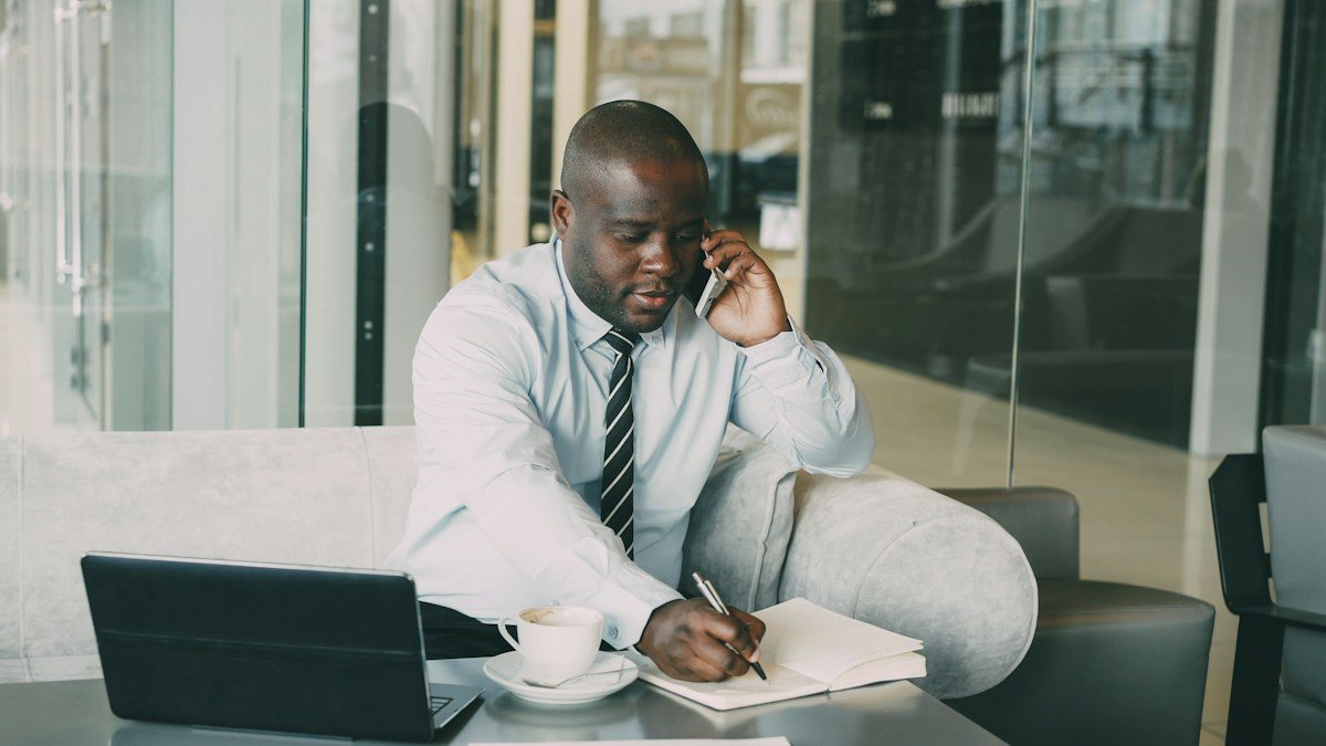Trader writing a trading risk management checklist in a notebook beside a laptop