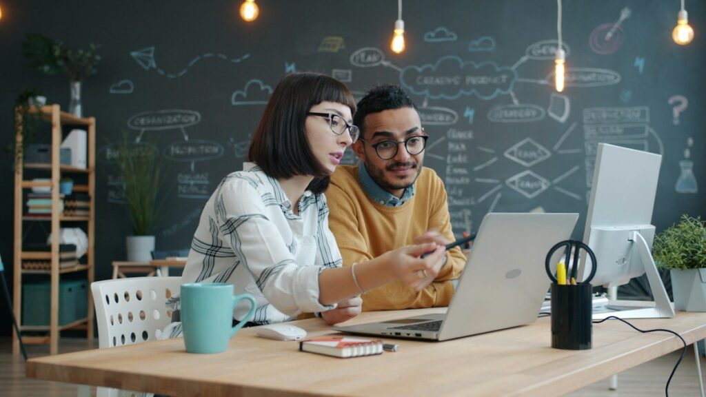 Two colleagues looking at a laptop at a desk