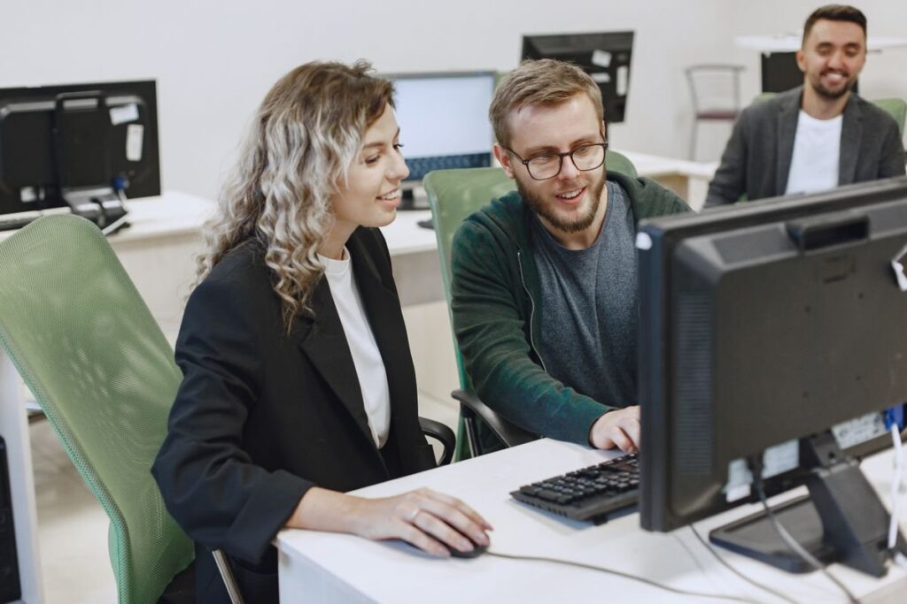 Three colleagues smiling at computer screens in an office