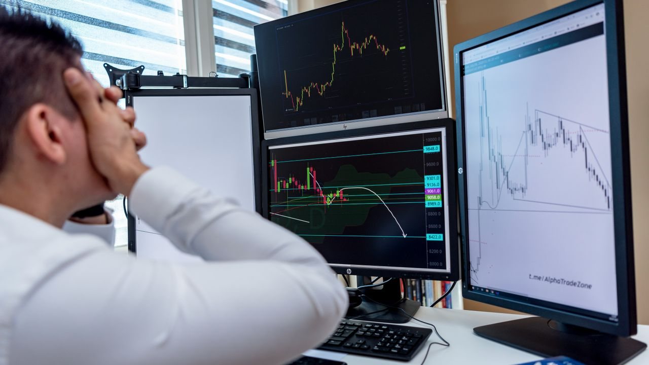 Man with his hand on his head at a desk of chart monitors