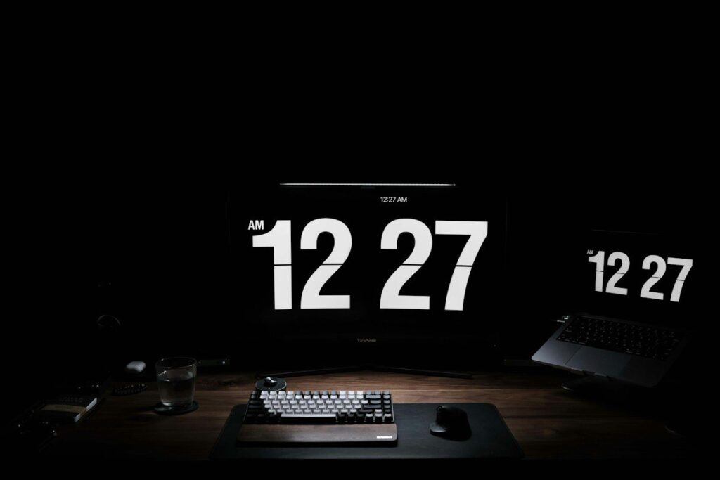 Desk clock display beside a keyboard in a dark room