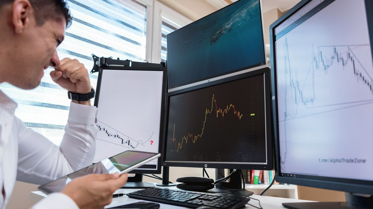 Trader at a desk with several monitors showing price charts