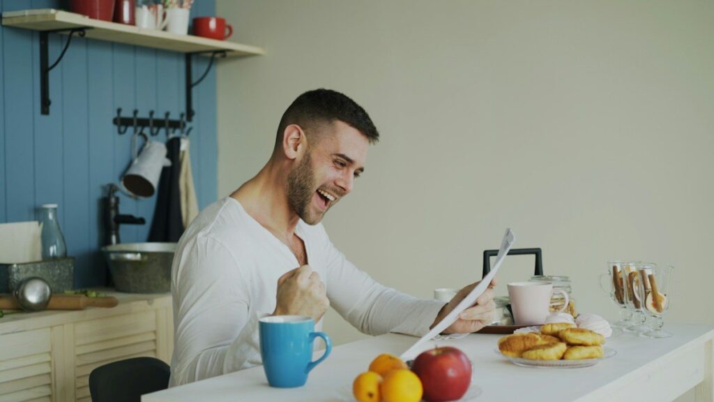 Man smiling as he reads papers at a kitchen table